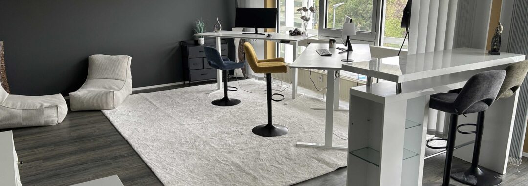 Büro mit mehreren Arbeitsplätzen, einem Tisch und Stühlen in neutralen Farben und einem Teppich.