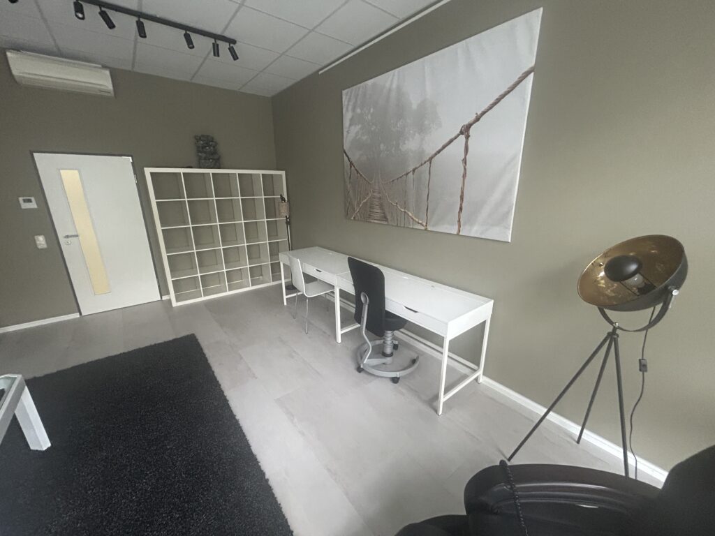 Ein Büro mit einem weißen Schreibtisch, einem schwarzen Bürostuhl und einer Wand mit einem großen Bild einer Hängebrücke.