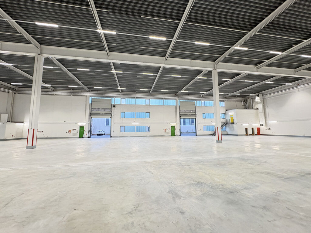 Große, leere Lagerhalle mit hohen Decken und großen Fenstern für Tageslicht.