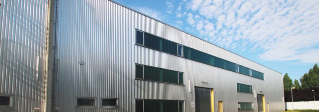 Industriegebäude mit silberner Metallfassade und großen Fenstern in einem klaren Himmel.