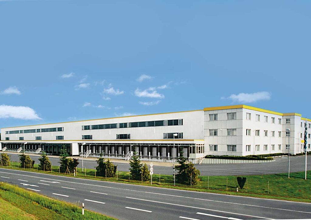 Moderne Büro- und Lagergebäude mit mehreren Fenstern und einem großen Eingang an einer Straße.